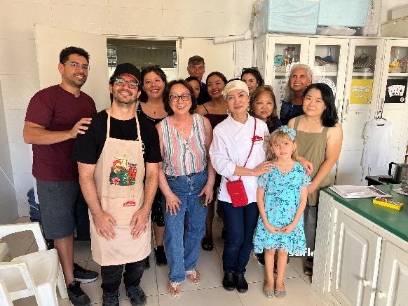 Grupo de participantes posa ao lado da chef responsável pela oficina de culinária, reunidos em uma cozinha.