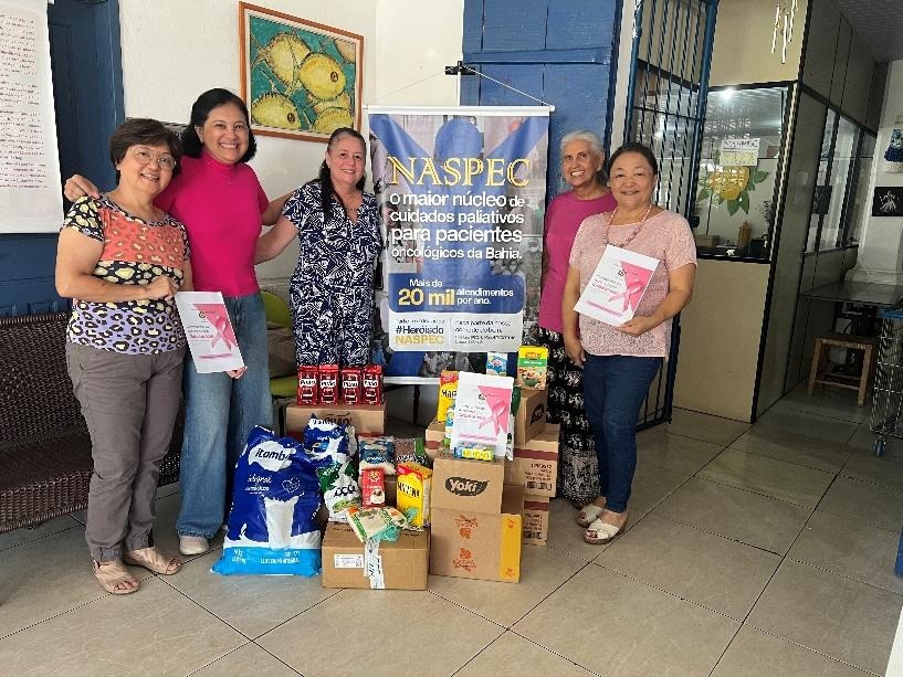 Grupo de mulheres associadas a entidades nipo-brasileiras posa ao lado de caixas e sacolas com alimentos arrecadados para o NASPEC, em ação solidária do Outubro Rosa.