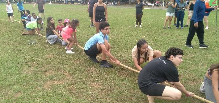 Crianças, adolescentes e adultos participam de provas tradicionais do Undokai, incluindo o Tsunahiki (cabo-de-guerra), em área aberta e gramada, promovendo integração e espírito de equipe.